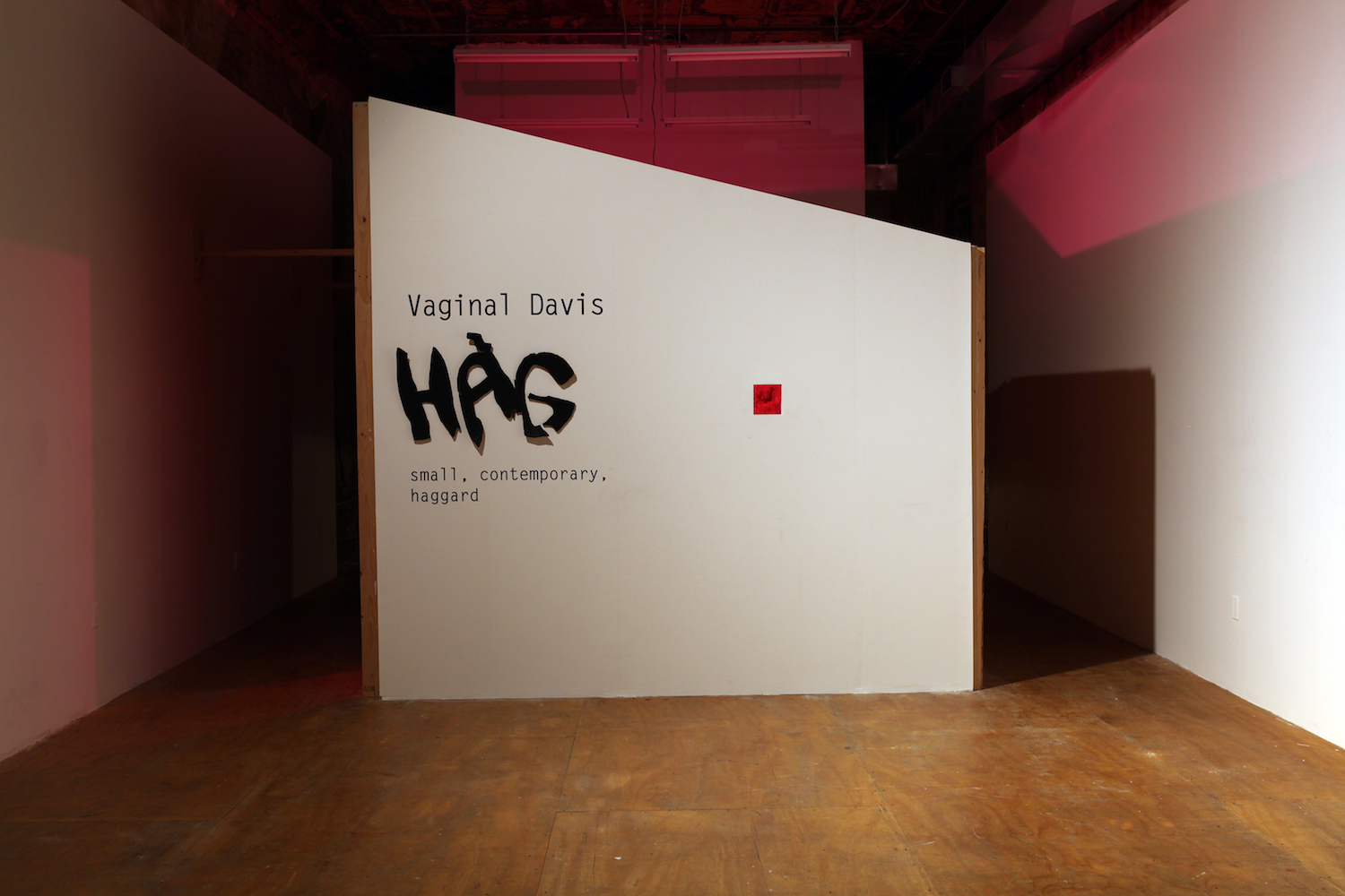 Vaginal Davis, *HAG – small, contemporary, haggard*, 2012. Ames room: wood, sheetrock; vinyl letters, cardboard, pink light bulb